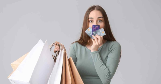A woman holding up multiple credit cards and several shopping bags