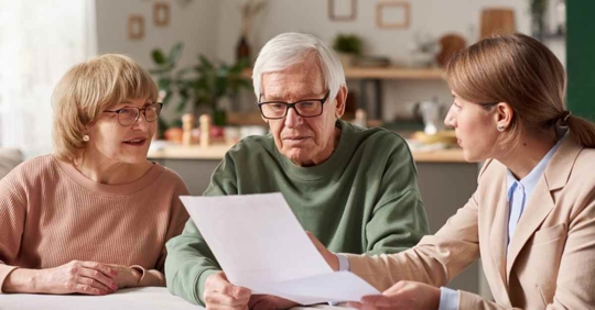 An older man and woman sitting near another woman who is holding up a piece of paper.
