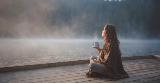 A woman drinking coffee while sitting out on a deck looking out at the water