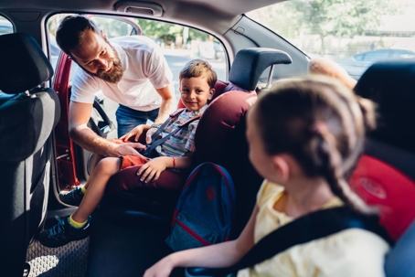 Dad buckling children into back seat of car