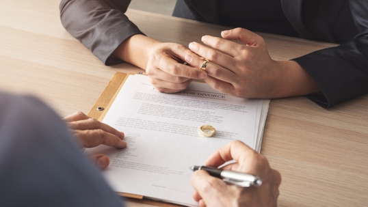 person signing divorce papers while another removes wedding ring