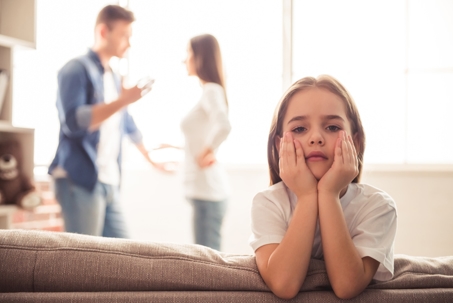 Child with head in hands while parents talk in background