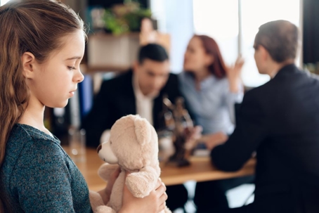 Child holding teddy bear and parents arguing