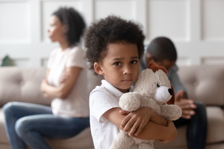 Child holding teddy bear and parents arguing