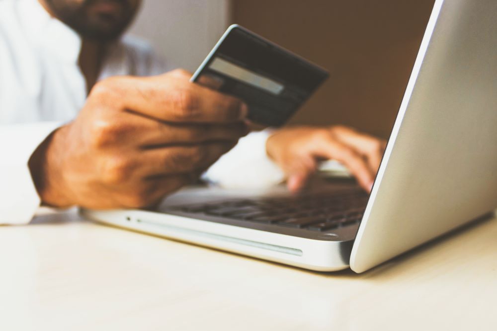 Close up of a man holding a credit card in one hand and typing on a laptop with the other.